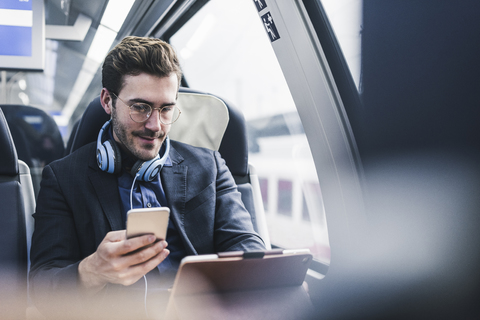 Geschäftsmann im Zug mit Handy, Kopfhörer und Tablet, lizenzfreies Stockfoto
