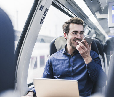 Lächelnder Geschäftsmann im Zug, der ein Mobiltelefon benutzt - UUF12632