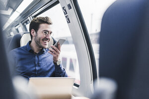 Happy businessman in train using cell phone - UUF12633