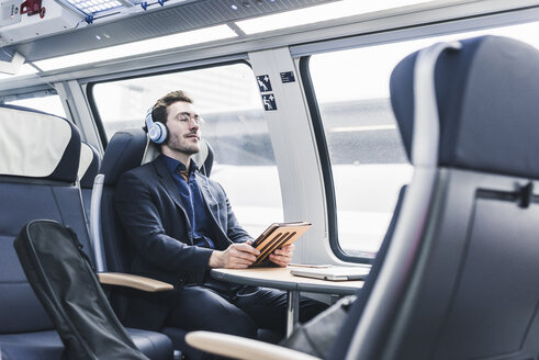 Geschäftsmann im Zug, der sich entspannt und Musik hört - UUF12634