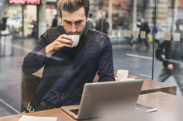 Young businessman in a cafe at train station with cup of coffee and laptop - UUF12640