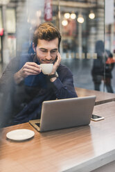 Young businessman in a cafe at train station with cup of coffee and laptop - UUF12642