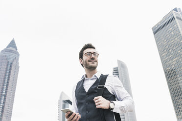 Germany, Frankfurt, confident young businessman with cell phone in the city - UUF12650