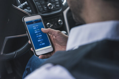 Man in car adjusting smart home devices via smartphone - UUF12654