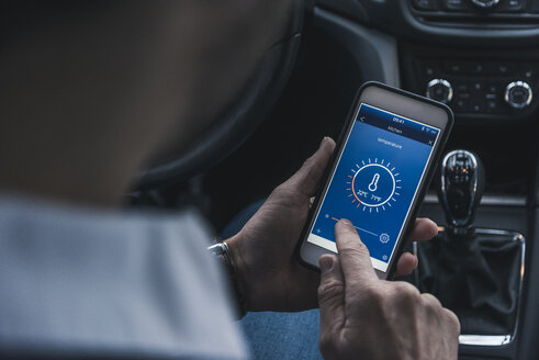 Man in car adjusting smart home device via smartphone - UUF12657