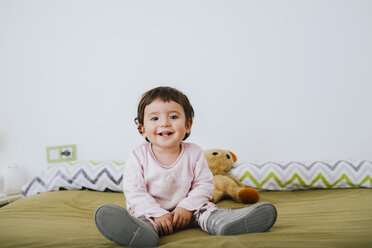 Porträt eines glücklichen kleinen Mädchens auf dem Bett sitzend - GEMF01871