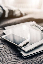 Stack of three mobile devices on bed - GIOF03858