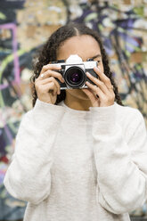 Germany, Berlin, young woman taking pictures with an old camera in front of graffiti - OJF00229