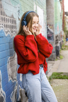 Deutschland, Berlin, lächelnde junge Frau, die mit Kopfhörern Musik hört - OJF00236