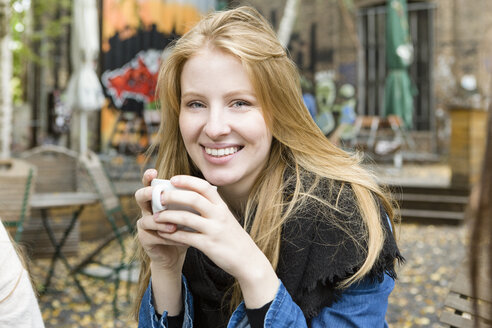 Deutschland, Berlin, Porträt einer glücklichen jungen Frau beim Kaffeetrinken in einem Straßencafé - OJF00243