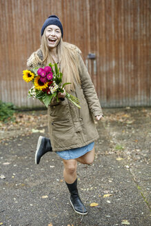 Porträt einer glücklichen jungen Frau, die einen Blumenstrauß im Hof hält - PESF00901