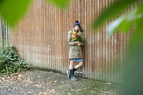 Porträt einer jungen Frau, die an einer Holzwand steht und einen Blumenstrauß hält - PESF00902