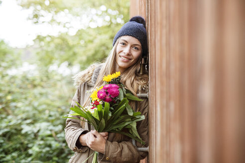 Porträt einer lächelnden jungen Frau, die einen Blumenstrauß im Freien hält - PESF00903