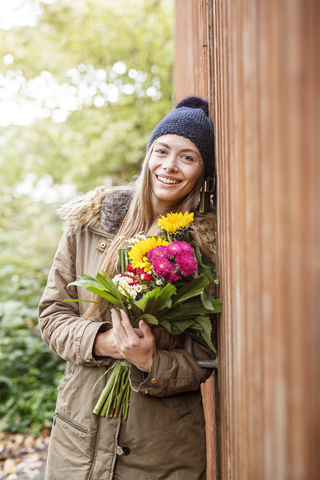 Porträt einer lächelnden jungen Frau, die einen Blumenstrauß im Freien hält, lizenzfreies Stockfoto