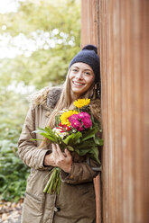 Portrait of smiling young woman holding bunch of flowers outdoors - PESF00904