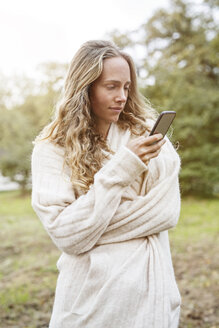 Blonde Frau in ländlicher Landschaft schaut auf ihr Handy - PESF00908