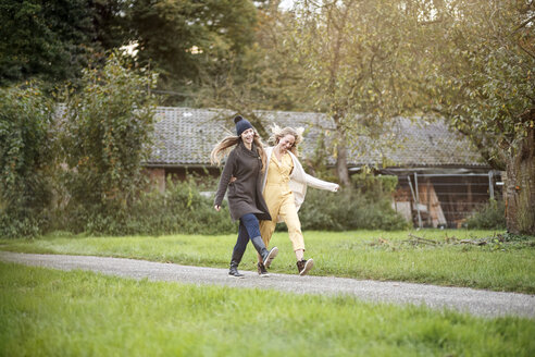 Zwei glückliche Frauen spazieren in ländlicher Landschaft - PESF00909