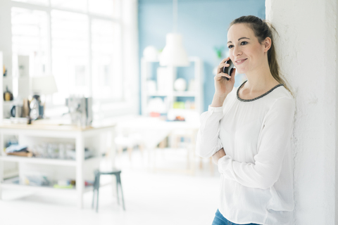 Portrait of smiling woman son the phone standing in a loft stock photo