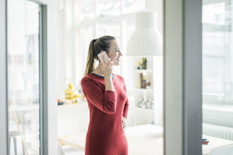 Lächelnde Frau am Telefon mit Blick aus dem Fenster, lizenzfreies Stockfoto