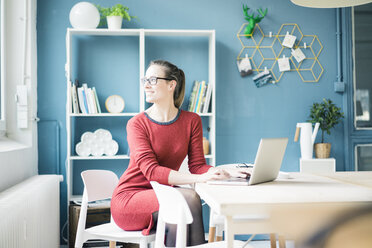 Smiling woman sitting at table with laptop looking out of window - MOEF00728