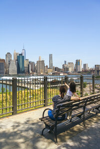 USA, New York, Brooklyn, Rückenansicht einer Frau und eines jungen Mädchens, die auf einer Bank sitzen und die Skyline von Manhattan von Brooklyn aus betrachten - DAPF00868