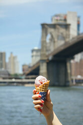 USA, New York, Brooklyn, Nahaufnahme einer Frau, die eine Erdbeereiswaffel in der Hand hält, mit der Brooklyn Bridge im Hintergrund - DAPF00870