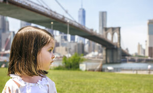USA, New York, Brooklyn, Porträt eines kleinen Mädchens im Park, das zur Seite schaut, mit der Brooklyn Bridge im Hintergrund - DAPF00873
