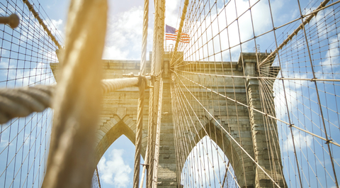 USA, New York, Brooklyn, Nahaufnahme der Brooklyn Bridge Metallkabel und Bögen mit amerikanischer Flagge an der Spitze, lizenzfreies Stockfoto