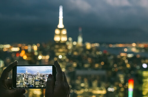 USA, Frau hält Smartphone in der Hand, während sie ein Foto von Manhattan bei Nacht macht - DAPF00885