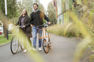 Smiling couple walking with bicycles on a lane - PESF00914