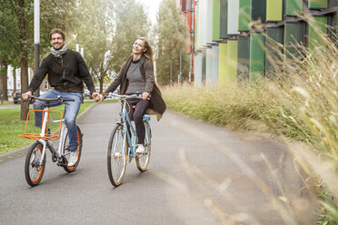Glückliches Paar beim Fahrradfahren Hand in Hand auf einer Fahrbahn - PESF00916