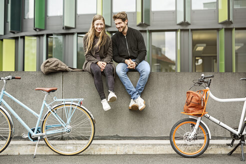 Glückliches Paar mit Fahrrädern auf einer Mauer sitzend - PESF00922