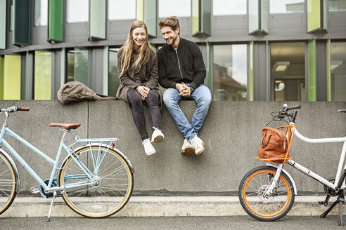 Happy couple with bicycles sitting on a wall - PESF00922