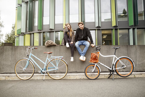 Glückliches Paar mit Fahrrädern auf einer Mauer sitzend - PESF00923