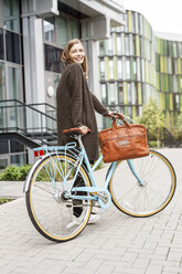 Smiling woman with bicycle standing in front of a building - PESF00935