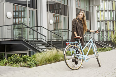 Smiling woman with bicycle standing in front of a building - PESF00937