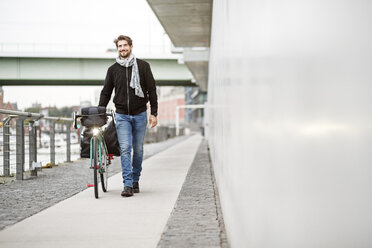 Lächelnder Mann, der ein Fahrrad auf einem Weg schiebt - PESF00938