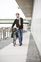 Smiling man pushing bicycle on a path - PESF00939