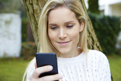 Porträt einer lächelnden blonden Frau, die im Freien auf ihr Handy schaut - FMKF04752