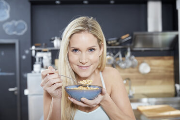 Portrait of smiling blond woman in the kitchen eating cereals - FMKF04755
