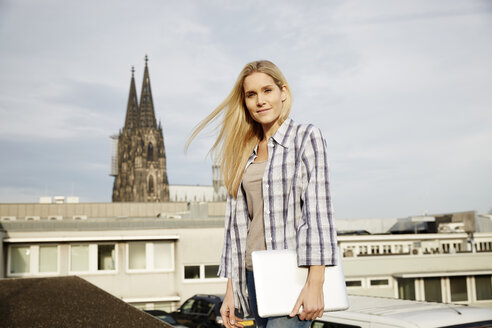 Deutschland, Köln, Porträt einer lächelnden blonden Frau mit Laptop - FMKF04761