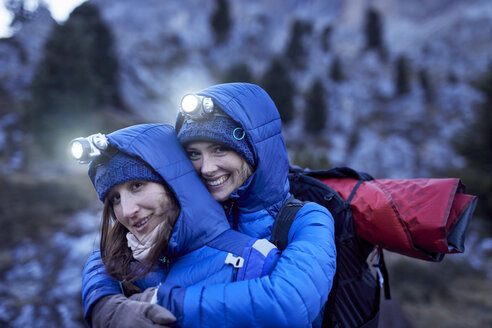 Two happy young women wearing headlamps embracing in the mountains - PNEF00457