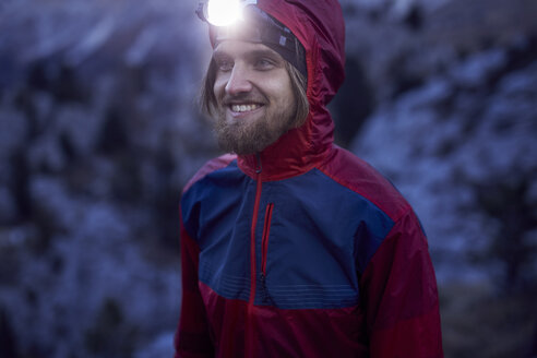 Portrait of smiling man wearing headlamp at dusk in the mountains - PNEF00459