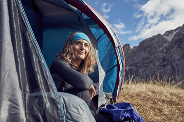 Lächelnde junge Frau sitzt im Zelt in den Bergen - PNEF00468