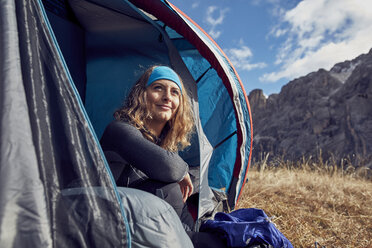 Smiling young woman sitting in tent in the mountains - PNEF00468