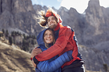 Glückliches junges Paar, das sich in den windigen Bergen umarmt - PNEF00482
