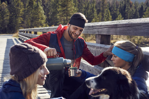 Gruppe von Freunden mit Hund wandernd rastend auf einer Brücke, lizenzfreies Stockfoto