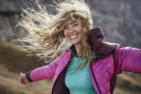 Glückliche junge Frau, die sich in den Bergen gegen den Wind lehnt, lizenzfreies Stockfoto