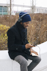 Italy, Milan, African american with smartphone, headphone and book - MAUF01281