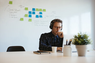 Businessman wearing headphones using laptop at desk in office - EBSF02077